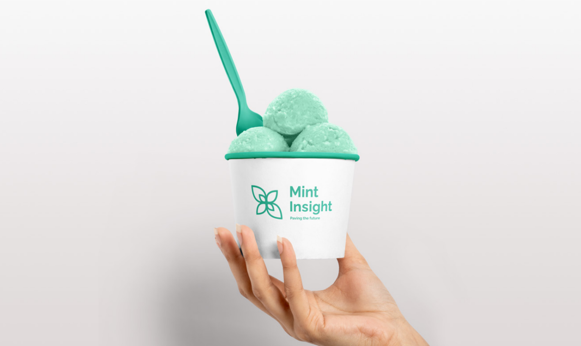 A person's hand holding a white ice cream cup with a green spoon. The cup contains three scoops of mint green ice cream and features the Mint Insight logo.