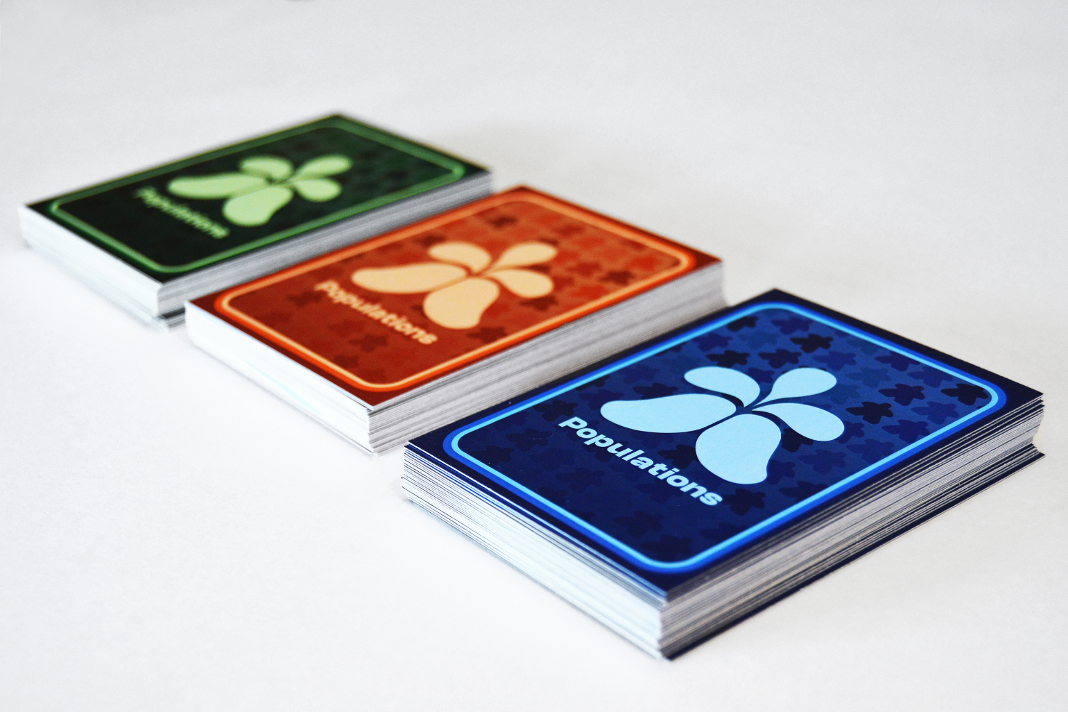 A stack of three different colored card decks from the Populations board game: green, orange, and blue