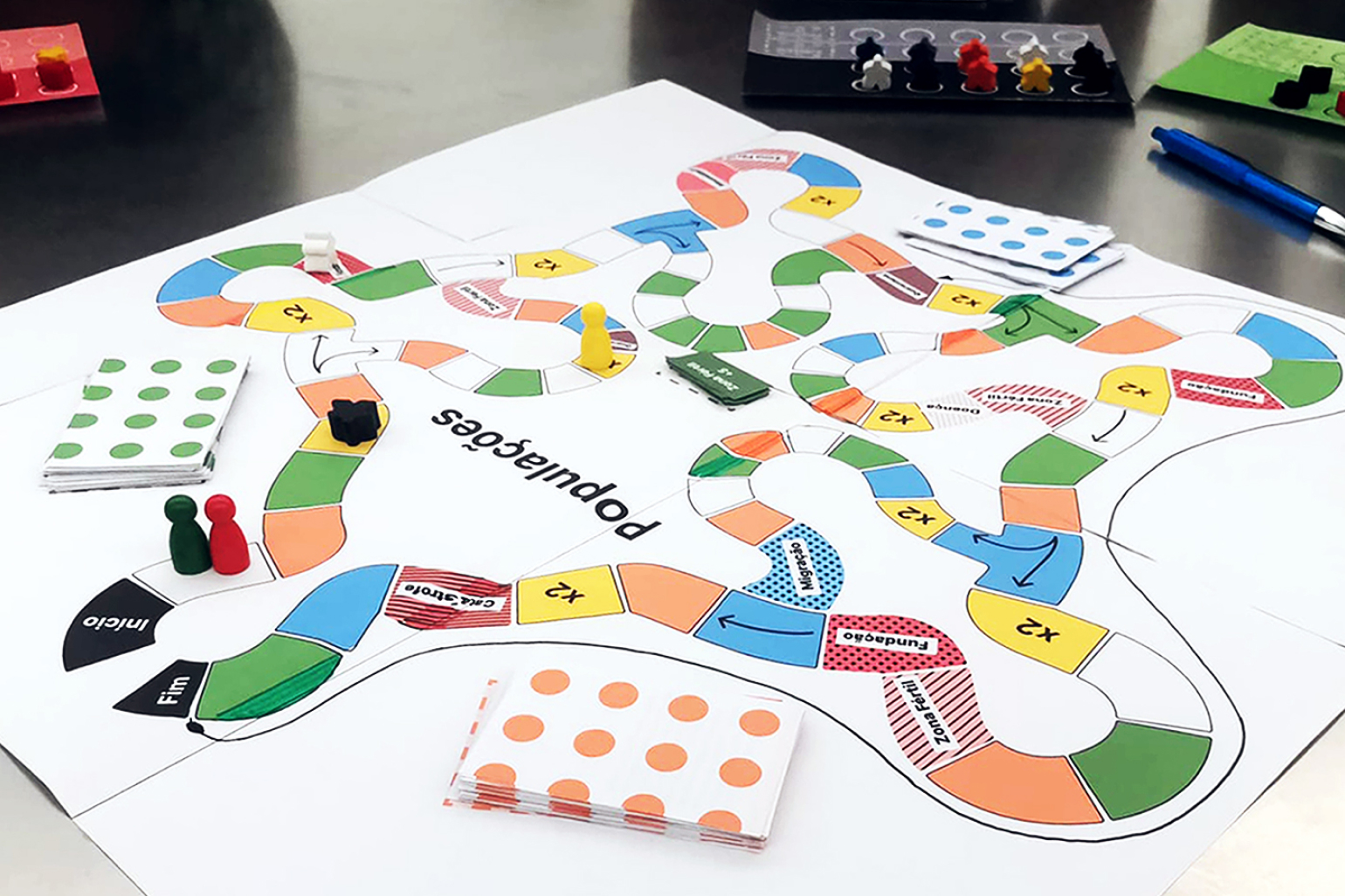 A low-fidelity paper prototype of the Populations board game, showing the game board layout, meeples, and cards